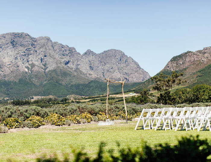 Outdoor wedding ceremony set up with white chairs and a wooden arch in the Cape Winelands